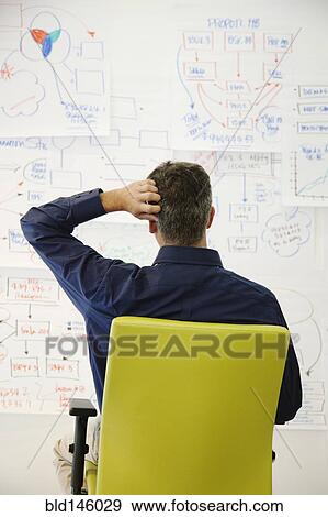 Confused businessman looking at paper drawings View Large Photo Image Stock Photo - Confused businessman looking at paper drawings. Fotosearch