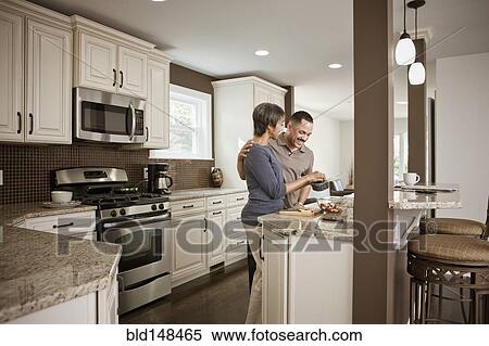 Stock Photography - Couple preparing meal together in kitchen. Fotosearch