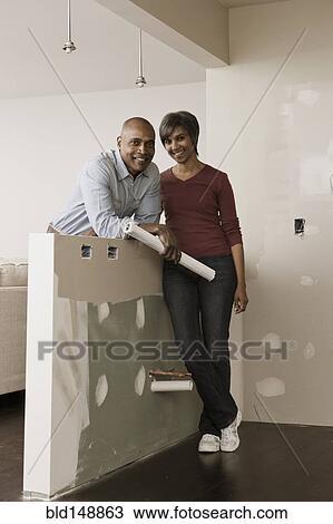 Stock Image - Couple standing in unfinished room with blueprints. Fotosearch