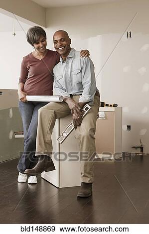Stock Photo - Couple with level and blueprints in unfinished room. Fotosearch