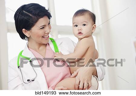 Stock Image - Doctor holding serious baby in doctor's office. Fotosearch