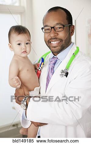 Doctor holding serious baby in doctor's office View Large Photo Image Stock Photography - Doctor holding serious baby in doctor's office. Fotosearch