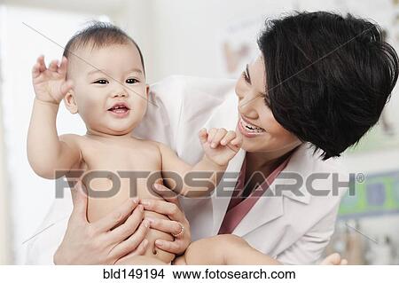 Picture - Doctor holding smiling baby in doctor's office. Fotosearch