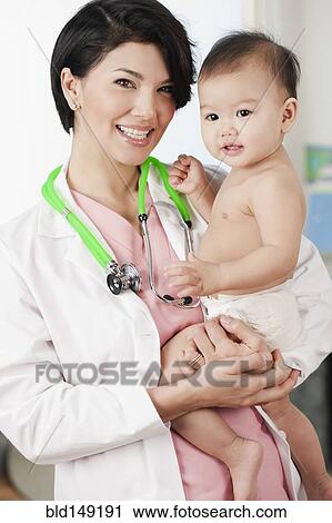 Stock Image - Doctor holding smiling baby in doctor's office. Fotosearch