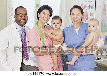 Stock Image - Doctor with nurses holding babies in doctor's office. Fotosearch