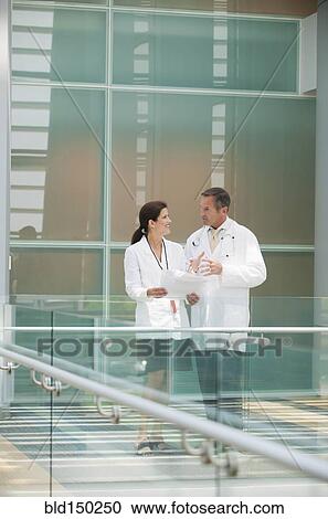 Stock Image - Doctors talking together near hospital railing. Fotosearch