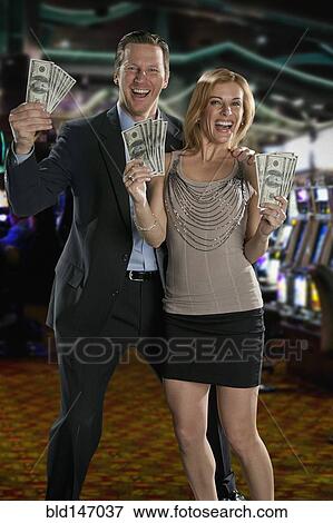 Stock Photo - Excited Caucasian couple holding cash winnings in casino. Fotosearch