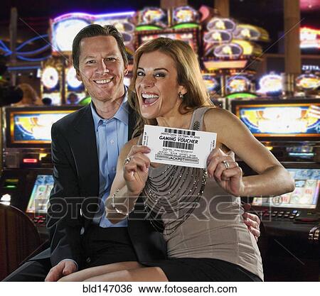 Stock Photograph - Excited Caucasian couple holding gaming voucher in casino. Fotosearch