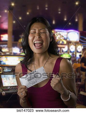 Stock Image - Excited Chinese woman holding gaming voucher in casino. Fotosearch
