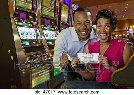Stock Photo - Excited couple displaying gaming voucher in casino. Fotosearch