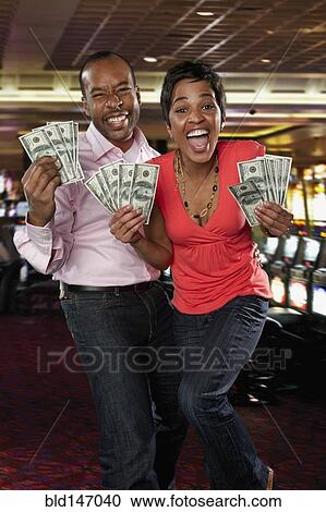 Stock Image - Excited couple holding cash winnings in casino. Fotosearch