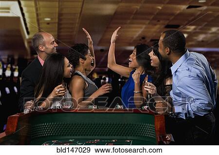 Stock Photo - Excited friends gambling at craps table in casino. Fotosearch