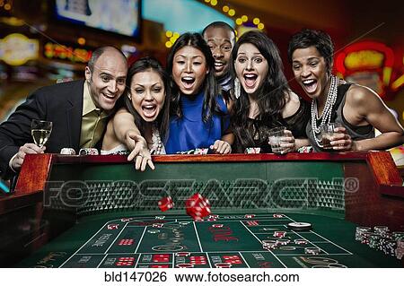 Stock Photograph - Excited friends gambling at craps table in casino. Fotosearch