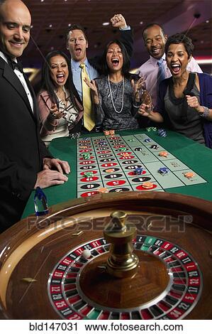 Stock Image - Excited friends gambling at roulette table in casino. Fotosearch