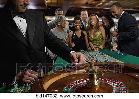 Stock Image - Excited friends gambling at roulette table in casino. Fotosearch
