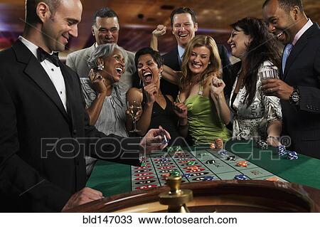 Stock Image - Excited friends gambling at roulette table in casino. Fotosearch