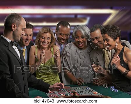 Stock Image - Excited friends gambling at roulette table in casino. Fotosearch