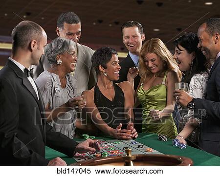 Stock Photography - Excited friends gambling at roulette table in casino. Fotosearch