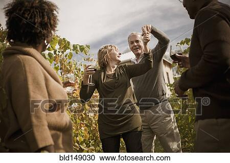 Stock Image - Friends drinking wine in vineyard. Fotosearch
