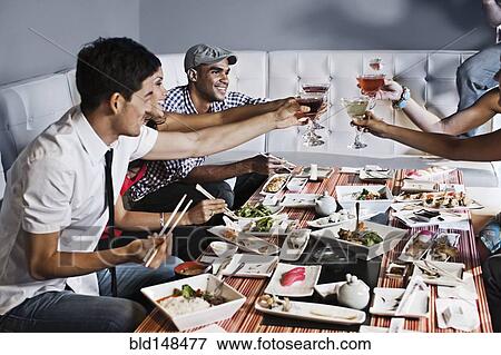 Stock Photo - Friends toasting and eating together in restaurant. Fotosearch
