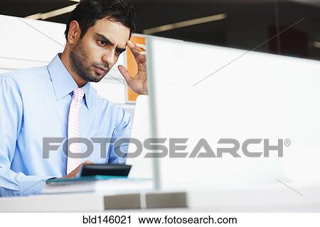 Stock Image - Frowning businessman sitting at desk. Fotosearch