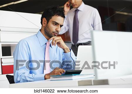 Stock Image - Frowning businessman sitting at desk. Fotosearch