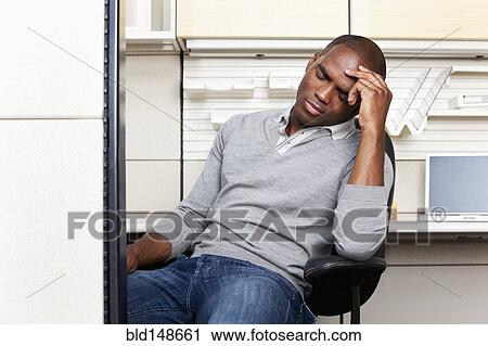 Stock Image - Frustrated mixed race businessman sitting in office cubicle. Fotosearch