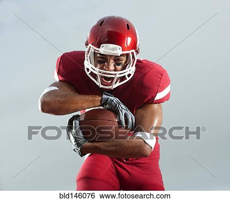 Stock Photograph - Grimacing Black football player carrying football. Fotosearch