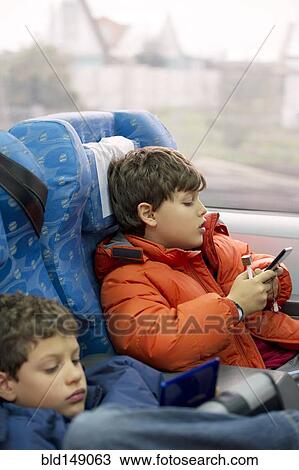 Stock Image - Hispanic brothers playing video games on train. Fotosearch