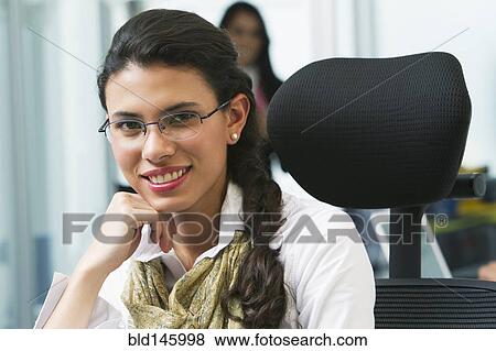 Stock Photo - Hispanic businesswoman sitting at desk in office. Fotosearch