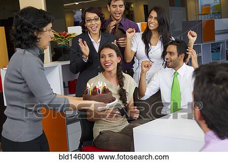 Stock Photo - Hispanic co-workers surprising businesswoman with birthday cake. Fotosearch