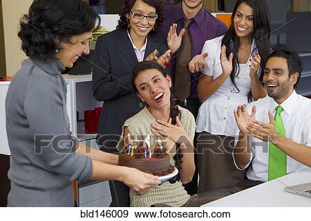 Stock Photo - Hispanic co-workers surprising businesswoman with birthday cake. Fotosearch