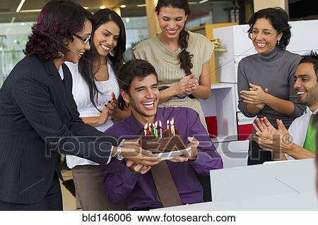 Stock Photograph - Hispanic co-workers surprising businessman with birthday cake. Fotosearch