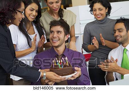 Stock Photography - Hispanic co-workers surprising businessman with birthday cake. Fotosearch