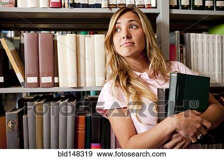 Stock Photo - Hispanic college student holding books in library. Fotosearch