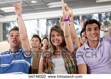 Stock Image - Hispanic college students raising arms in classroom. Fotosearch