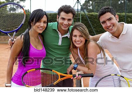 Stock Photo - Hispanic couples smiling near tennis court net. Fotosearch