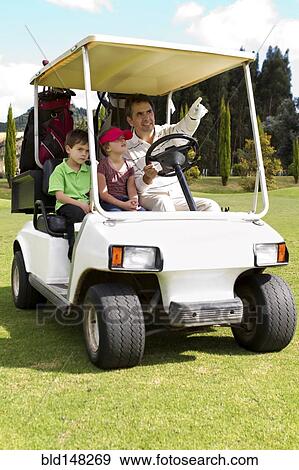 Stock Photo - Hispanic father and children riding in golf cart. Fotosearch