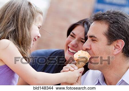 Picture - Hispanic girl giving father a bite of her ice cream cone. Fotosearch