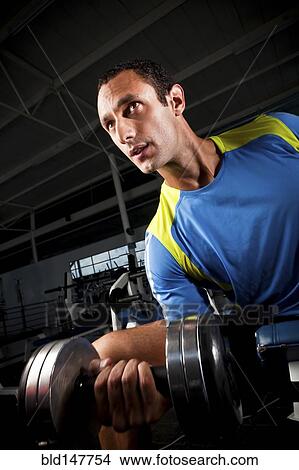 Picture - Hispanic man lifting weights in health club. Fotosearch