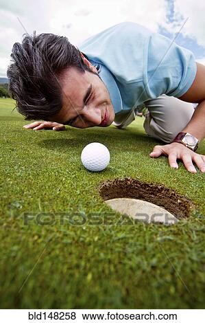 Hispanic man looking at golf ball near cup View Large Photo Image Stock Photo - Hispanic man looking at golf ball near cup. Fotosearch