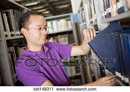 Stock Image - Hispanic man searching for book in library. Fotosearch