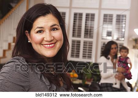 Stock Image - Hispanic woman in living room with family. Fotosearch