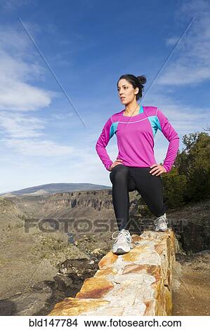 Picture - Hispanic woman stretching on rock wall in remote area. Fotosearch