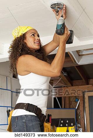 Stock Image - Hispanic woman using cordless drill. Fotosearch