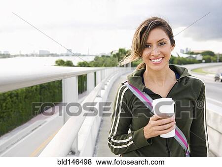 Stock Photo - Hispanic woman walking outdoors with coffee. Fotosearch