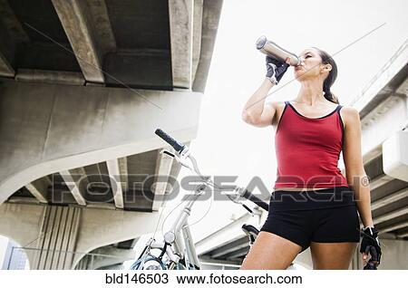 Stock Image - Hispanic woman with bicycle drinking water. Fotosearch