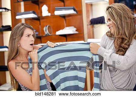 Stock Image - Hispanic women fighting over shirt in store. Fotosearch