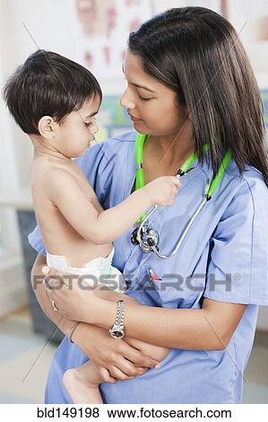Stock Photo - Indian nurse holding baby in doctor's office. Fotosearch