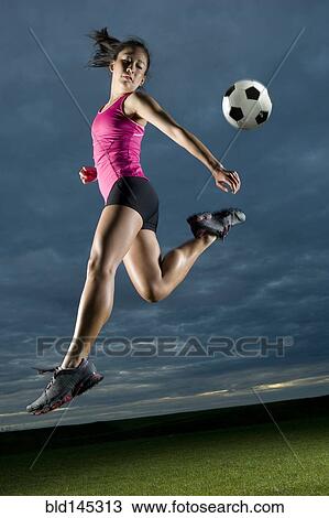 Stock Image - Japanese woman playing soccer at night. Fotosearch